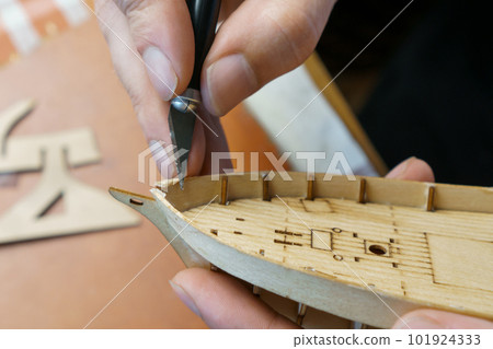 Hands man cutting out details for ship model with clerical knife from plywood. Process of building toy ship, handicraft. Hands man cutting out details for ship model with clerical knife from plywood. Process of building toy ship, handicraft. 101924333