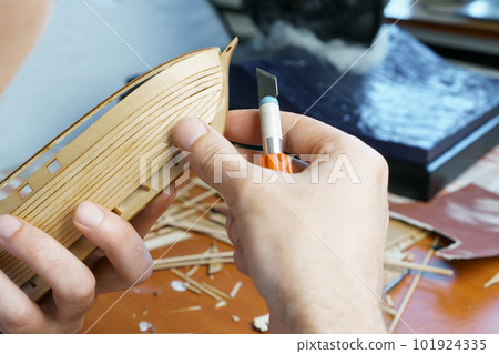 Hands man cutting out details for ship model with clerical knife from plywood. Process of building toy ship, handicraft. Hands man cutting out details for ship model with clerical knife from plywood. Process of building toy ship, handicraft. 101924335