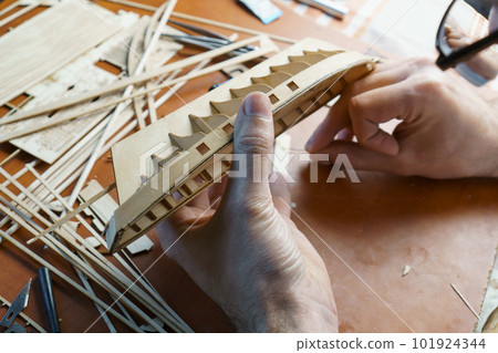 Hands of man gluing plywood details for ship model with glue, holding with fingers. Process of building toy ship 101924344
