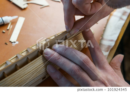 Hands of man gluing plywood details for ship model with glue, holding with fingers. Process of building toy ship Hands of man gluing plywood details for ship model with glue, holding with fingers. Process of building toy ship 101924345
