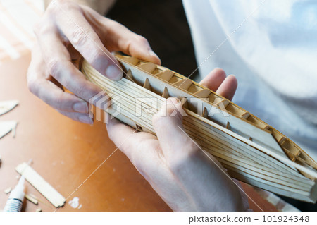 Hands of man gluing plywood details for ship model with glue, holding with fingers. Process of building toy ship 101924348