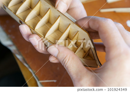 Hands of man gluing plywood details for ship model with glue, holding with fingers. Process of building toy ship 101924349