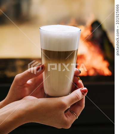 A female hand holding a cup of coffee against fireplace 101925666