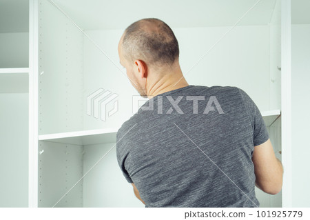 Male hold shelf, inserting and securing it to supports, assembling white dresser or wardrobe Male hold shelf, inserting and securing it to supports, assembling white dresser or wardrobe 101925779
