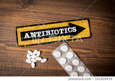 Antibiotics Concept. Yellow direction sign with arrow and text. Pills on a wooden background Antibiotics Concept. Yellow direction sign with arrow and text. Pills on a wooden background 101926459