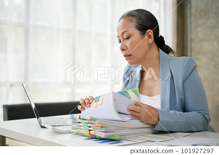 Smart senior businesswoman working in her office room with stack of papers. 101927297