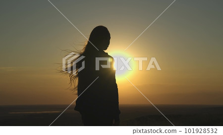 young girl looks at sunset and prays, religious person, her hair is flying in wind in glare of the sun, to believe in goodness, a woman's dream of love, to think and ask for forgiveness from heaven 101928532