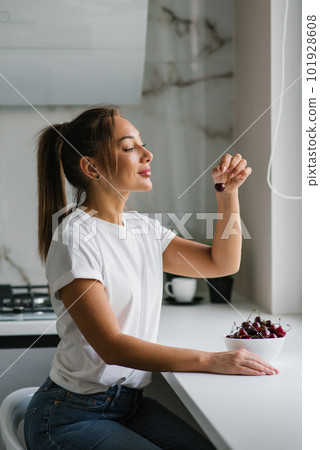 Young woman is eating a sweet cherry. Portrait of a beautiful girl with a cherry in the kitchen. 101928608