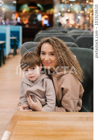 Portrait of a beautiful young mother and a four-year-old son in her arms. The family is sitting in a cafe on a chair Portrait of a beautiful young mother and a four-year-old son in her arms. The family is sitting in a cafe on a chair 101928610