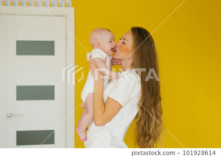 Loving mother holds her newborn baby in her arms at home. A vivid portrait of a happy mother kissing her little son. 101928614