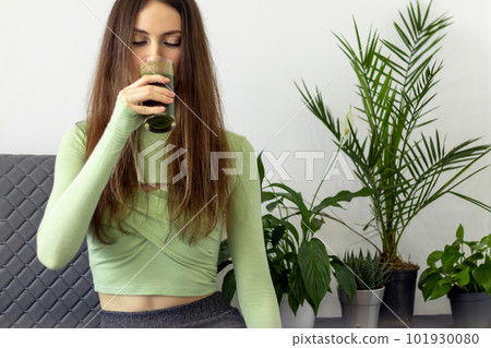 A beautiful young woman with a beautiful figure drinks the green juice of wheat sprout Vitgrass plants. A beautiful young woman with a beautiful figure drinks the green juice of wheat sprout Vitgrass plants. 101930080