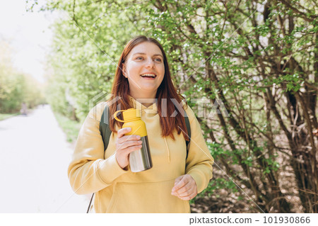Happy redhead Woman drinking water from water bottle or hot drink from yellow thermos on nature background. Smile pretty girl with freedom time Happy redhead Woman drinking water from water bottle or hot drink from yellow thermos on nature background. Smile pretty girl with freedom time 101930866