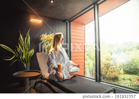 Woman in white bathrobe lying on sofa and relaxing with orange cocktail at home. 101932357