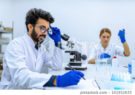 Health care researchers working in science laboratory microscoping making notes of his investigation 101932635