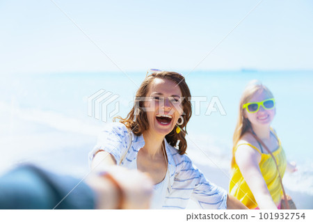smiling modern mother and teenage daughter at beach walking 101932754