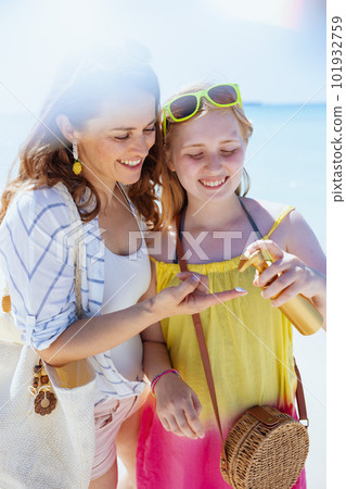 smiling mother and teenage daughter at beach using sunscreen 101932759