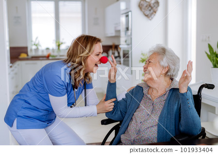 Nurse with clown nose having fun with her senior woman client. 101933404