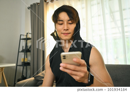 Young sportsman using smartphone on couch, resting after morning workouts at home Young sportsman using smartphone on couch, resting after morning workouts at home 101934184