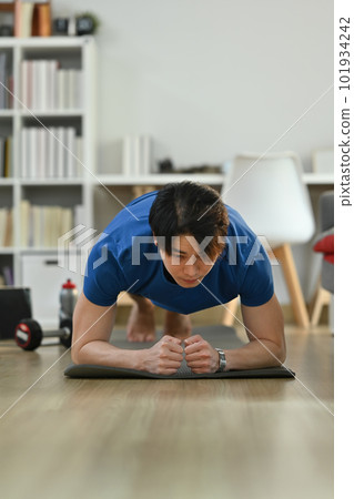 Sporty asian man wearing doing plank position while exercising in cozy home interior. Healthy lifestyle, sport and motivation concept Sporty asian man wearing doing plank position while exercising in cozy home interior. Healthy lifestyle, sport and motivation concept 101934242