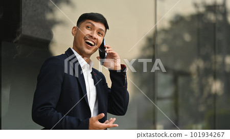 Portrait of adult businessman in formalwear standing outside building and talking on mobile phone 101934267