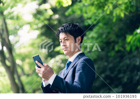 Businessman operating a smartphone in nature 101936193