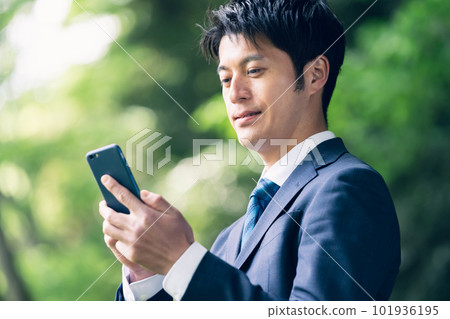 Businessman operating a smartphone in nature 101936195