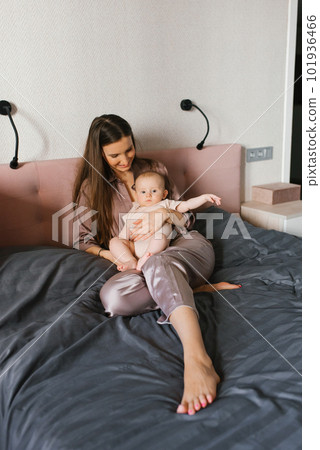 Mom with a baby in her arms sits in the bedroom on the bed. 101936466