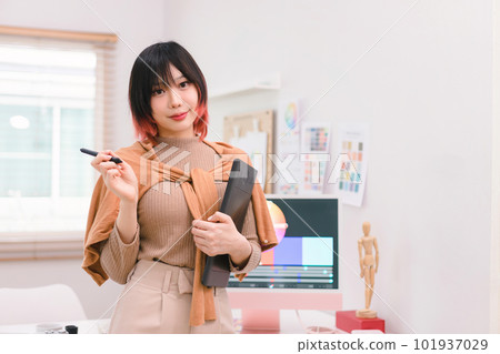 A portrait of a beautiful, professional, and confident millennial creative and stylish young female freelance designer hands holding a tablet and stylus pen while standing at her desk in office. 101937029
