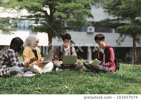 A multiethnic group of asian university students is seen studying together while sitting on the grass near the campus. A multiethnic group of asian university students is seen studying together while sitting on the grass near the campus. 101937074