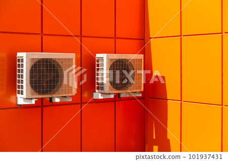 Two air compressors installation on orange wall outside. 101937431