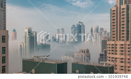 Dubai skyscrapers covered by morning fog in business bay district during sunrise timelapse. 101939748