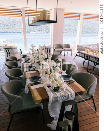 Laid festive table for guests in a restaurant with panoramic windows overlooking the sea Laid festive table for guests in a restaurant with panoramic windows overlooking the sea 101941158