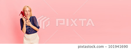 Banner with funny woman talking through shoe with heel instead of telephone with frightening, shocked face over pink studio background. Copy space for ad, text Banner with funny woman talking through shoe with heel instead of telephone with frightening, shocked face over pink studio background. Copy space for ad, text 101941690