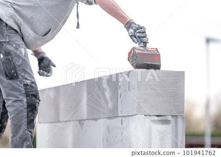 the mason applies glue to the concrete forms. construction of a wall of concrete bricks the mason applies glue to the concrete forms. construction of a wall of concrete bricks 101941762