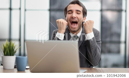 Excited businessman sitting at table with laptop and celebrating success 101942006