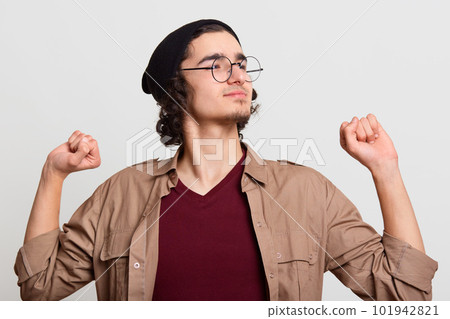Black haired sleepy calm guy doing stretch, exercising, looking aside, posing isolated over light grey background, having delighted facial expression, looks satisfied. Youth and activities concept. 101942821
