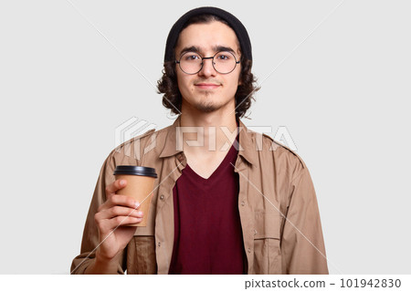 Handsome boy has curly hair, beard wears round transparent glasses, holds coffee to go, has break, communicates with friends, models against white background. People, lifestyle, drink concept 101942830