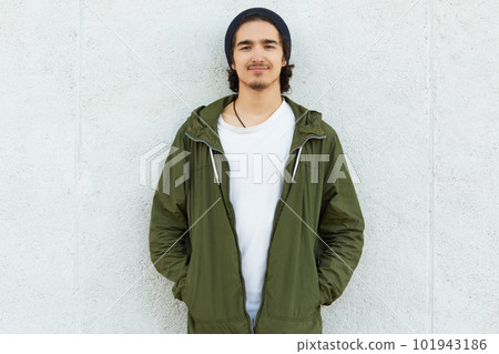 Image of delighted calm youngster standing straight outdoors, having pleasant facial expression. smiling calmly, looking directly at camera, putting hands into pockets. Street style concept. Image of delighted calm youngster standing straight outdoors, having pleasant facial expression. smiling calmly, looking directly at camera, putting hands into pockets. Street style concept. 101943186