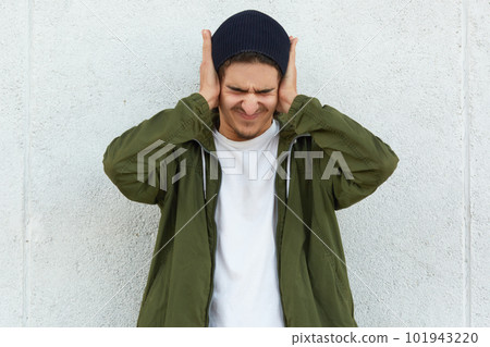 Annoyed upset angry young man closing his eyes, putting his hands on head, feeling bad, covering from noise, having headache, being in bad mood, wearing casual clothes. Health problems concept. 101943220