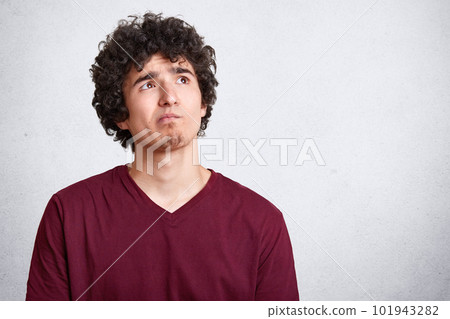 Portrait of attractive young man with curly hair thoughtfully looking at right upper corner over white background. Pensive guy in casual clothing thinks about something. Copyspace for promotion text. Portrait of attractive young man with curly hair thoughtfully looking at right upper corner over white background. Pensive guy in casual clothing thinks about something. Copyspace for promotion text. 101943282