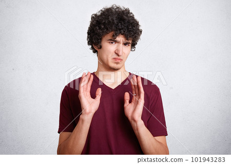Oh no, don`t bother me! Annoyed grumpy male with crisp hair, shows refusal gesture, poses against white background. Curly handsome teenager has dissatisfied expression, wears casual clothes. Oh no, don`t bother me! Annoyed grumpy male with crisp hair, shows refusal gesture, poses against white background. Curly handsome teenager has dissatisfied expression, wears casual clothes. 101943283