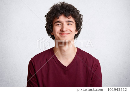 Positive male youngster with curly hair, looks joyfully at camera, has gentle smile, dressed in casual outfit, spends free time with girlfriend, isolated over white background. People and lifestyle 101943312