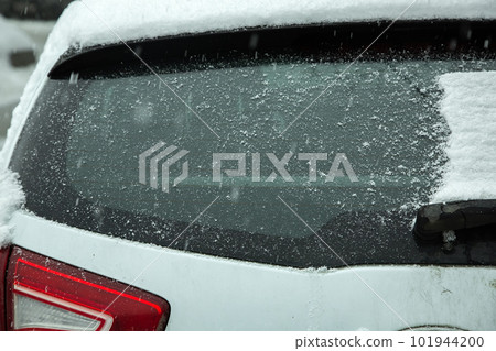 the glass of the car cleared of a snowdrift is again covered with a layer of snow in a winter blizzard, a close-up of the vehicle rear view. 101944200
