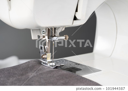 Modern sewing machine presser foot with gray fabric and thread, closeup Modern sewing machine presser foot with gray fabric and thread, closeup 101944387
