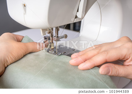 Female hands stitching white fabric on modern sewing machine at workplace in atelier Female hands stitching white fabric on modern sewing machine at workplace in atelier 101944389