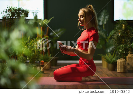 female in green living room doing yoga and using smartphone female in green living room doing yoga and using smartphone 101945843