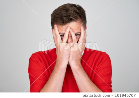 Scared man hides face behind palms, peeks through fingers, feels frightened Scared man hides face behind palms, peeks through fingers, feels frightened 101946707