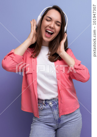 energetic brunette young woman in a shirt and jeans dances to the music from wireless headphones 101947307