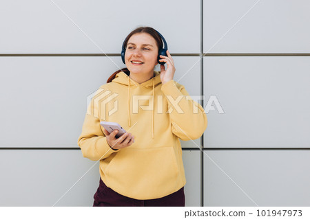 Closeup portrait of a lovely young girl listening to music through wireless earphones and singing on gray background. Music lover enjoying music. Woman record voice by mobie cell phone dictaphone Closeup portrait of a lovely young girl listening to music through wireless earphones and singing on gray background. Music lover enjoying music. Woman record voice by mobie cell phone dictaphone 101947973