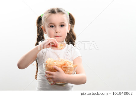 Little girl takes chips snacks with lard from a bowl and eats them, portrait on a white background and copy space 101948062